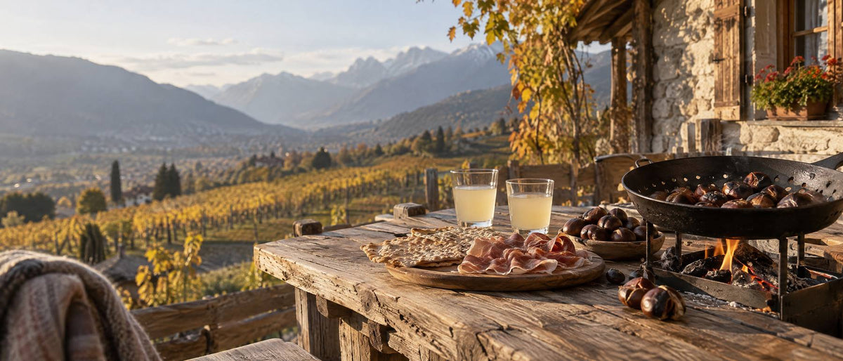 Holztisch im Freien mit gerösteten Kastanien, aufgeschnittenem Speck, Schüttelbrot und jungem Wein vor herbstlichen Weinbergen